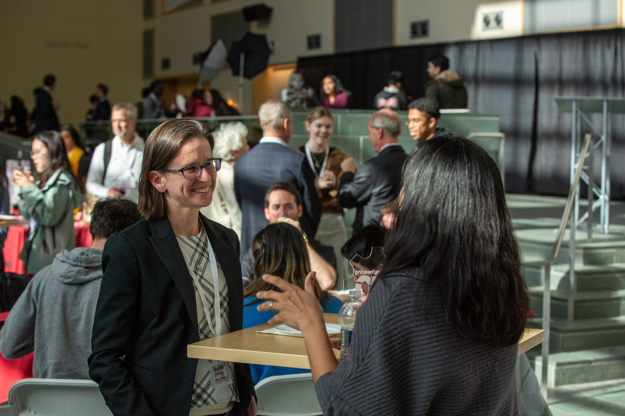 A woman smiles as she listens to another woman amid a crowd.