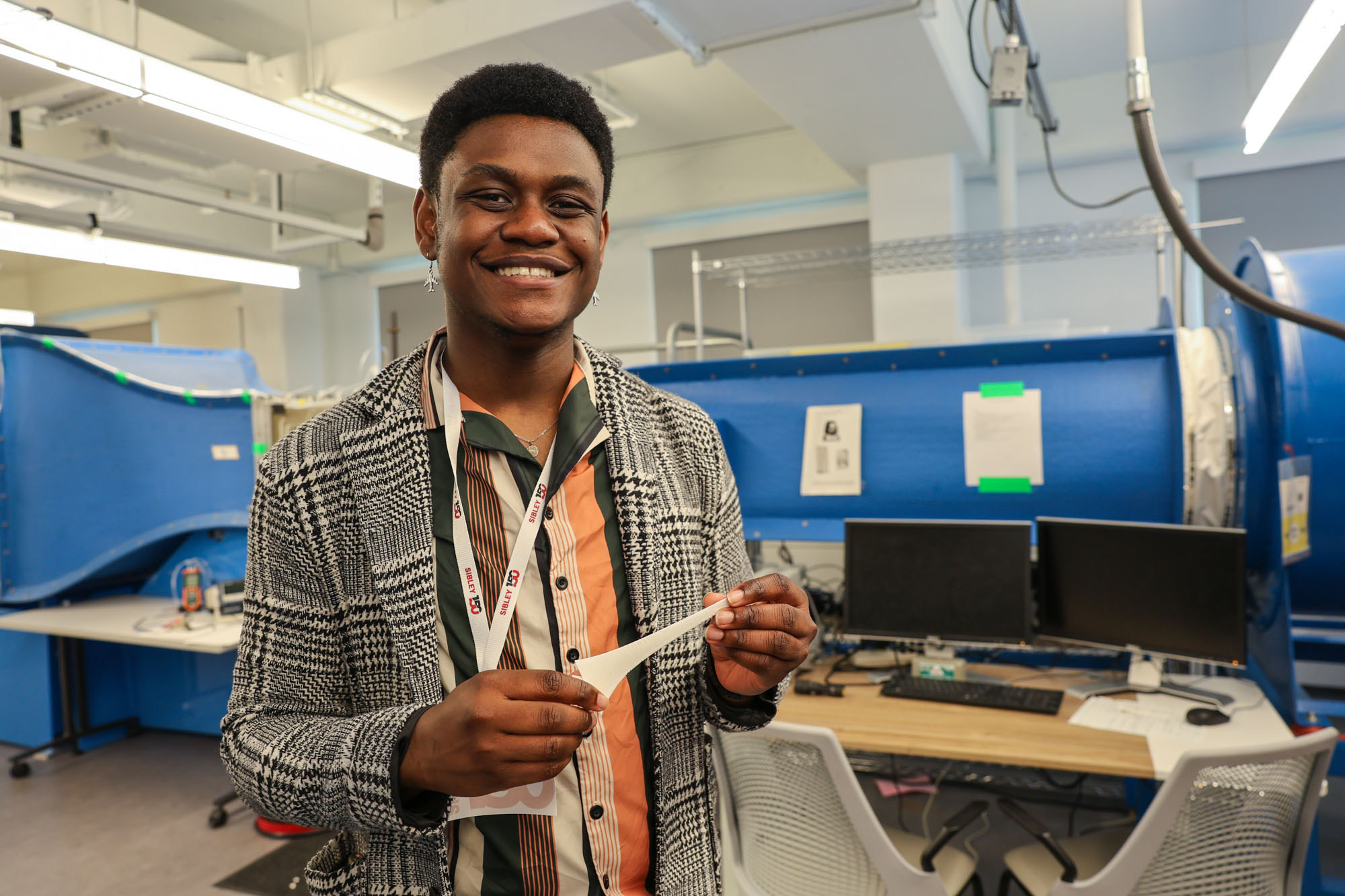 A male student holds a white object with two computer monitors in the background.