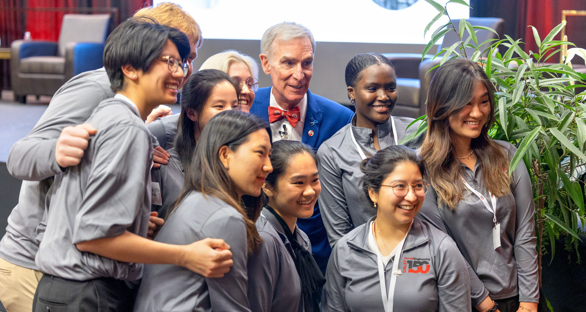 A man in a blue suit and red bowtie poses with nine students wearing grey shirts.