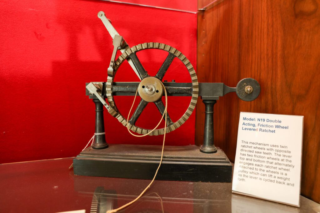 A Double Acting, Friction Wheel Levered Ratchet is shown in a display case