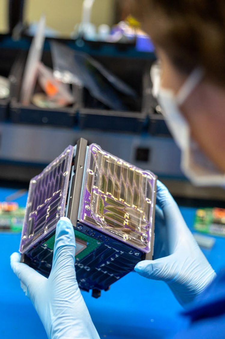 two hands hold a cubed satellite in a lab