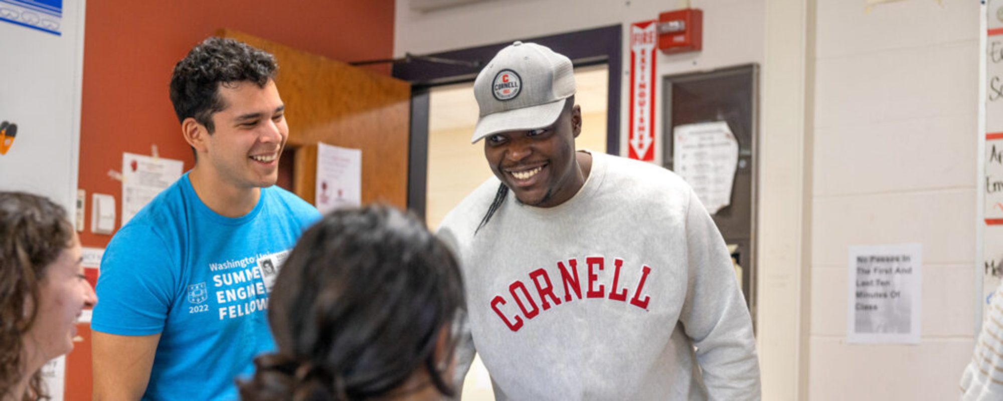 2 M.Eng. students smiling at students sitting down as part of Max Zhang Class Internet Of Things at Geneva High School