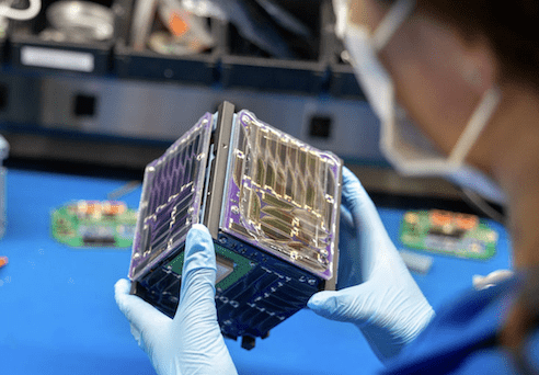 Gloved hands holding an 8-inch cubesat.