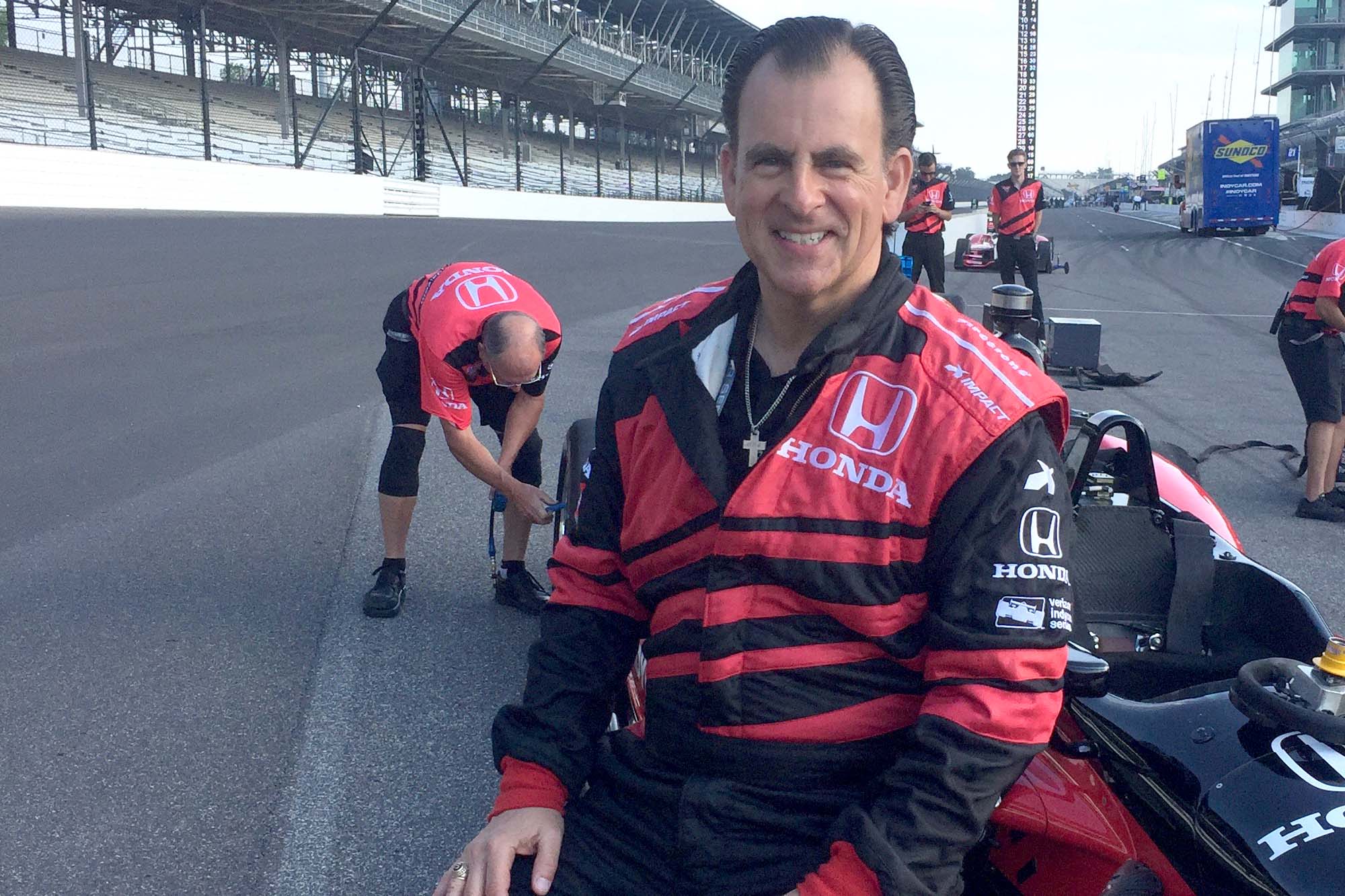 M.Eng. Alum Henio Arcangeli sits wearing race gear on racecar at Indianapolis racetrack.