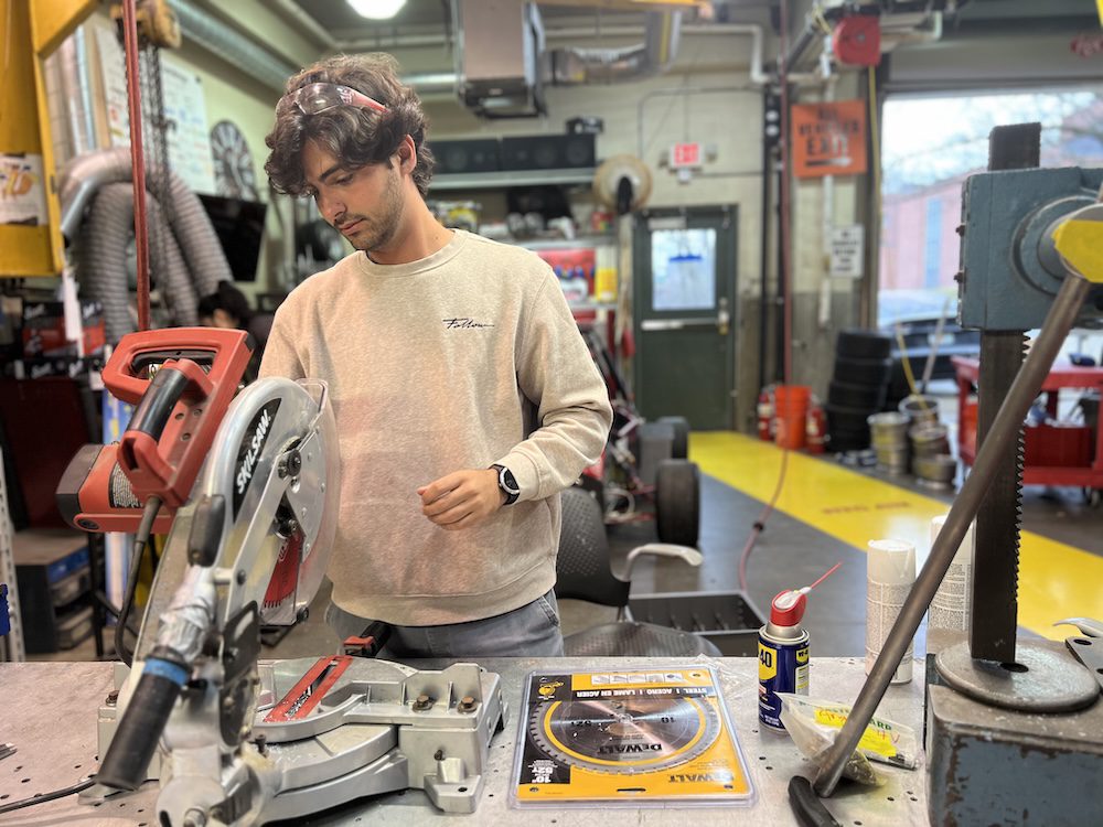 Student with safety glasses on his head makes an adjustment to a miter saw.