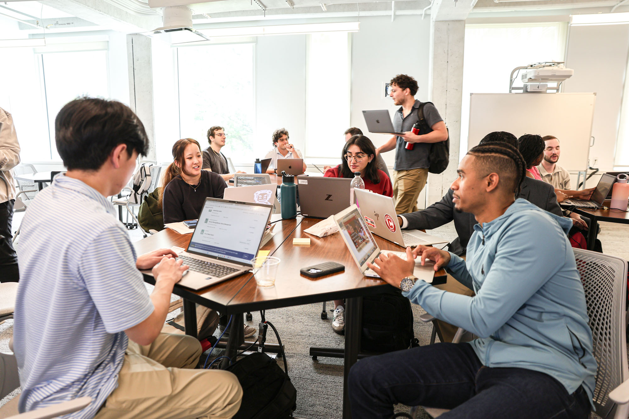 Distance learning students sitting around tables working on their laptops during their residential experience