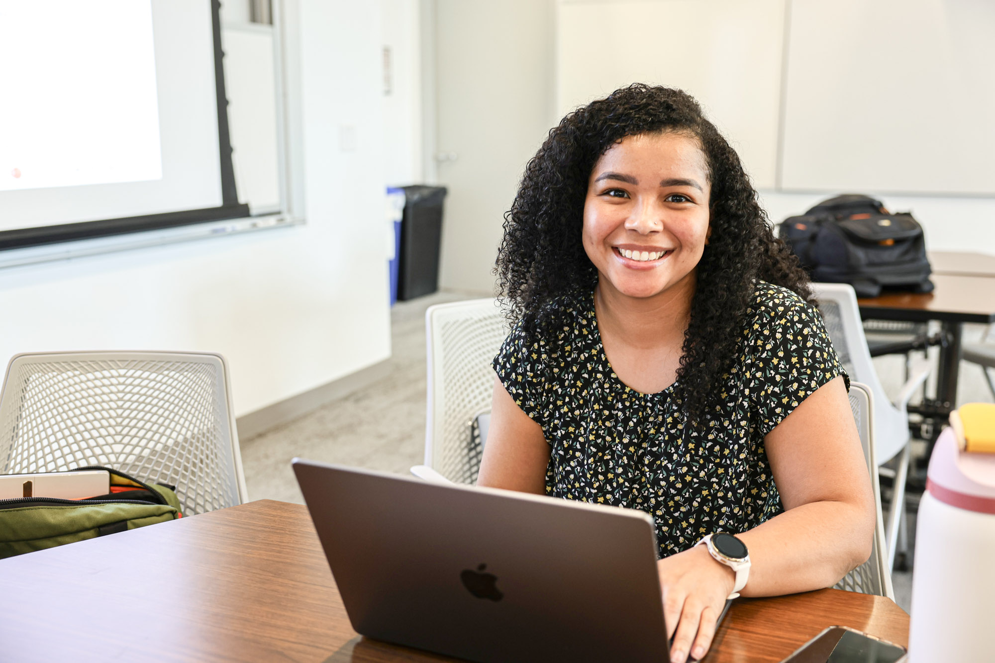 A smiling distance learning student sitting at a table working on their laptop during the residential experience