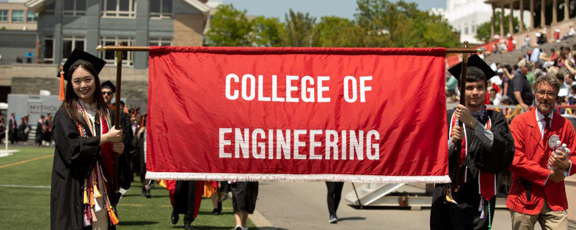 Students in graduation regalia during commencement. Large banner that says College of Engineering.