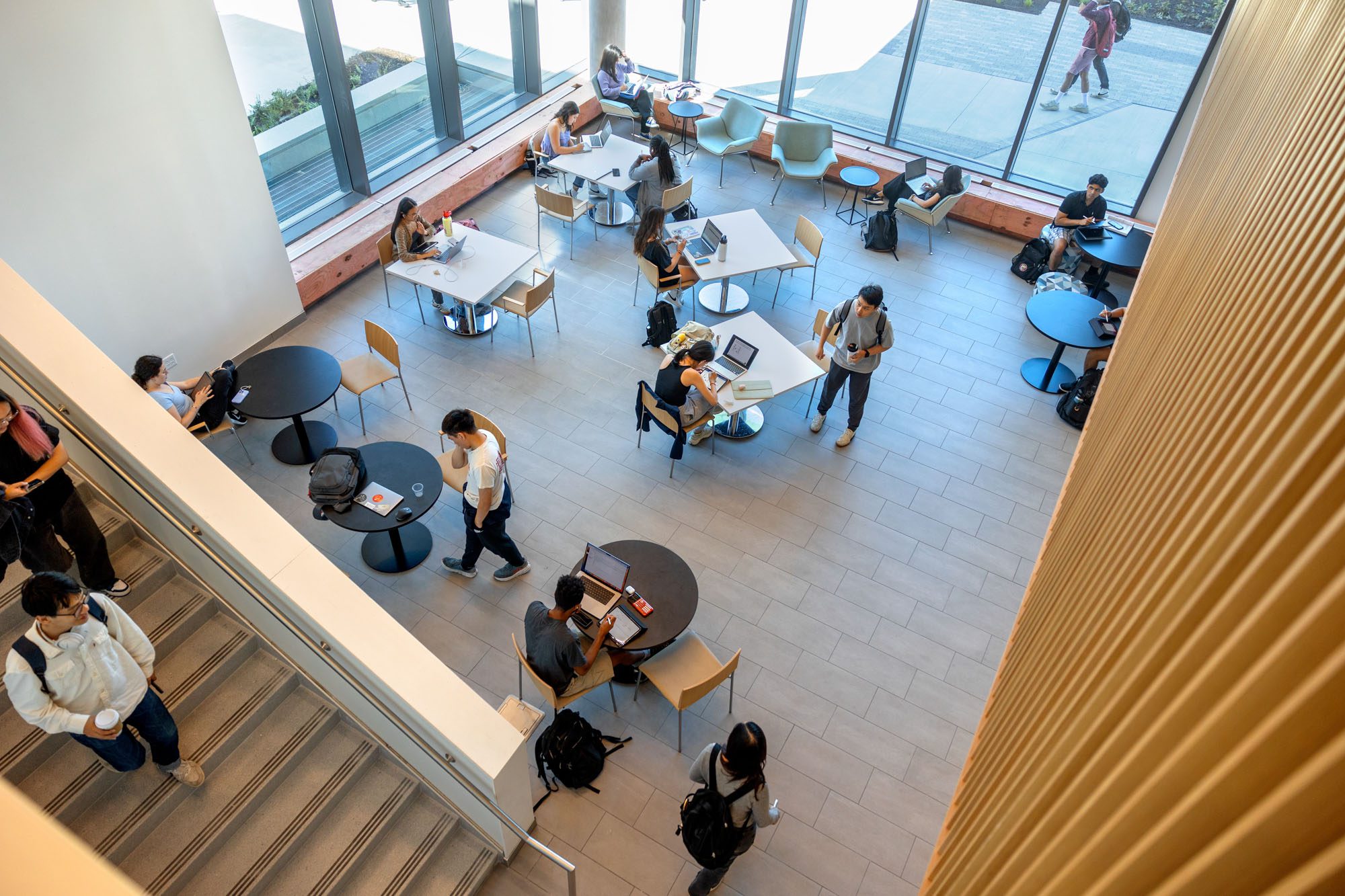 Students seated at tables on the first floor of Tang Hall by the large windows and entrance to the quad.