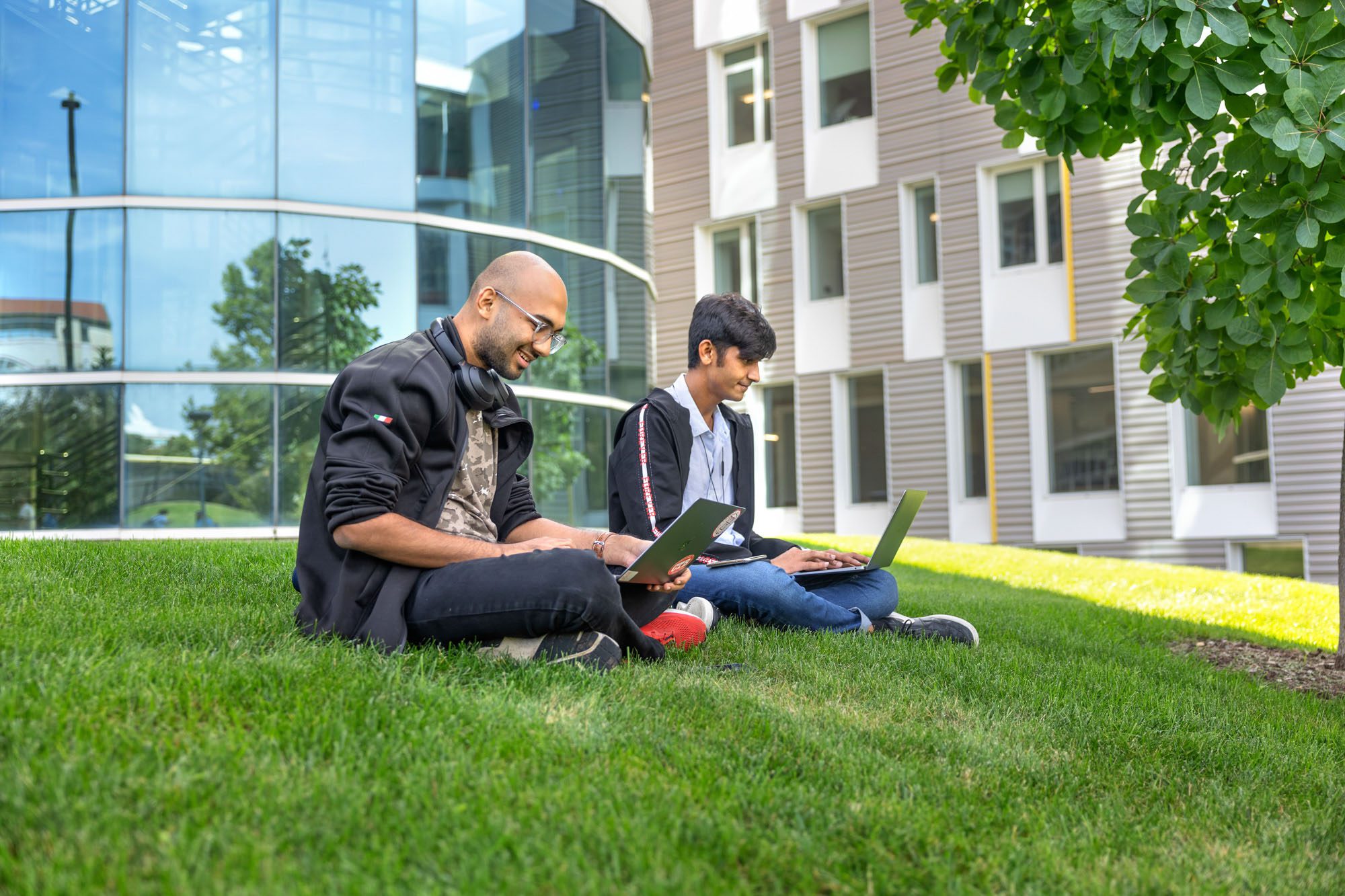 Two students smile working together outside Rhodes Hall on grassy lawn