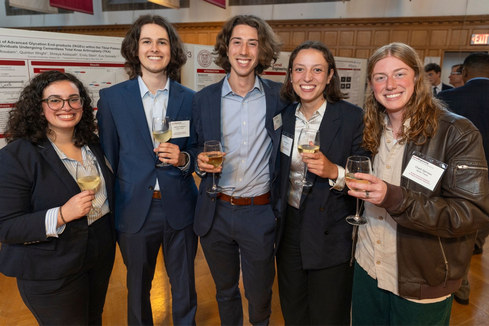 Students posing with glasses in their hand in front of a poster session in the background during the MSE awards gala