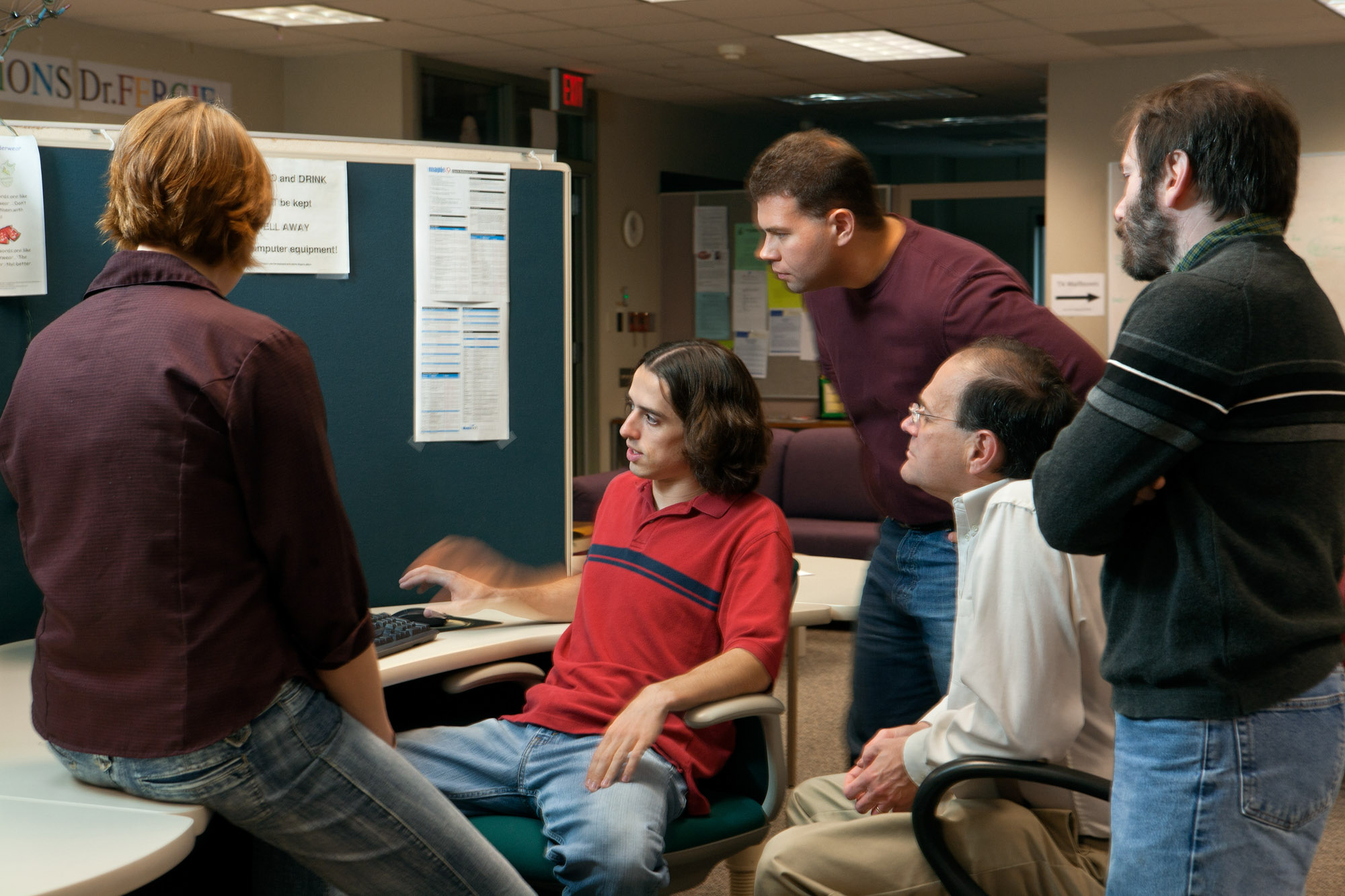 Five people look away from the camera and toward a computer screen.