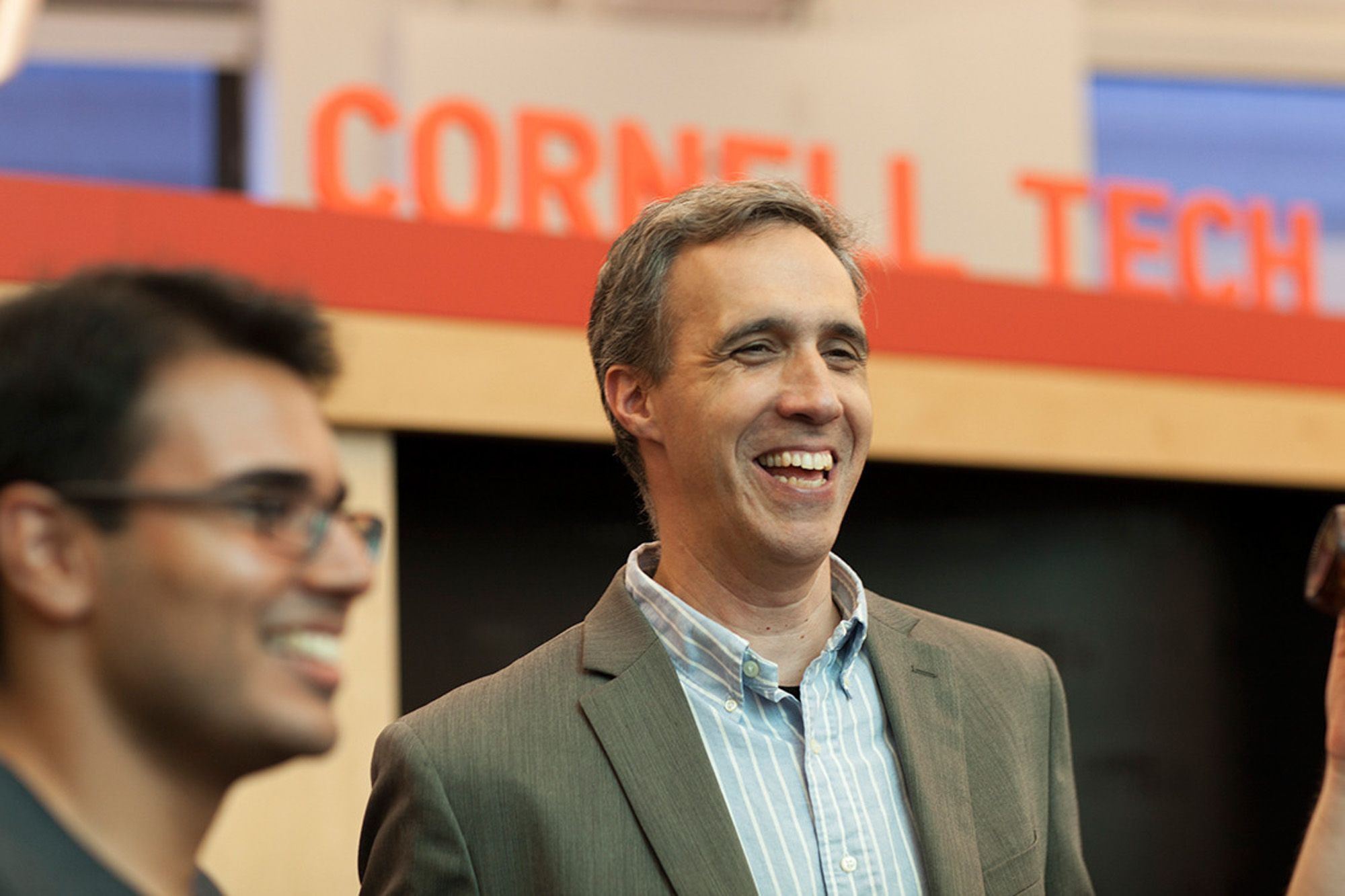 Dan Huttenlocher andanother man stand smiling in front of a red-lettered sign saying 