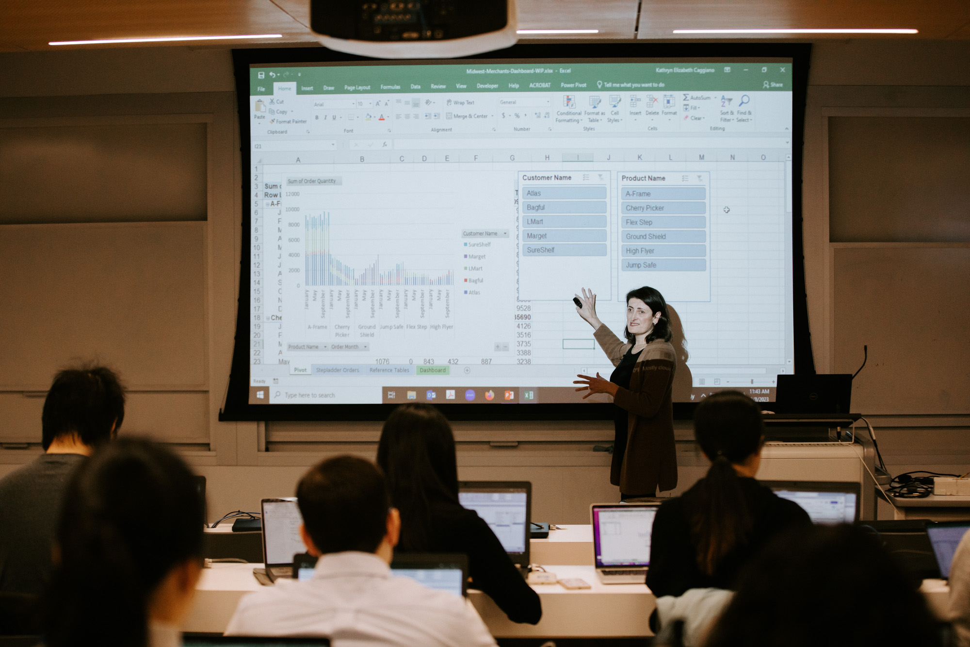 ORIE Professor Kathryn Caggiano lectures a class while standing in front of a screen that shows a graph and charts with data.