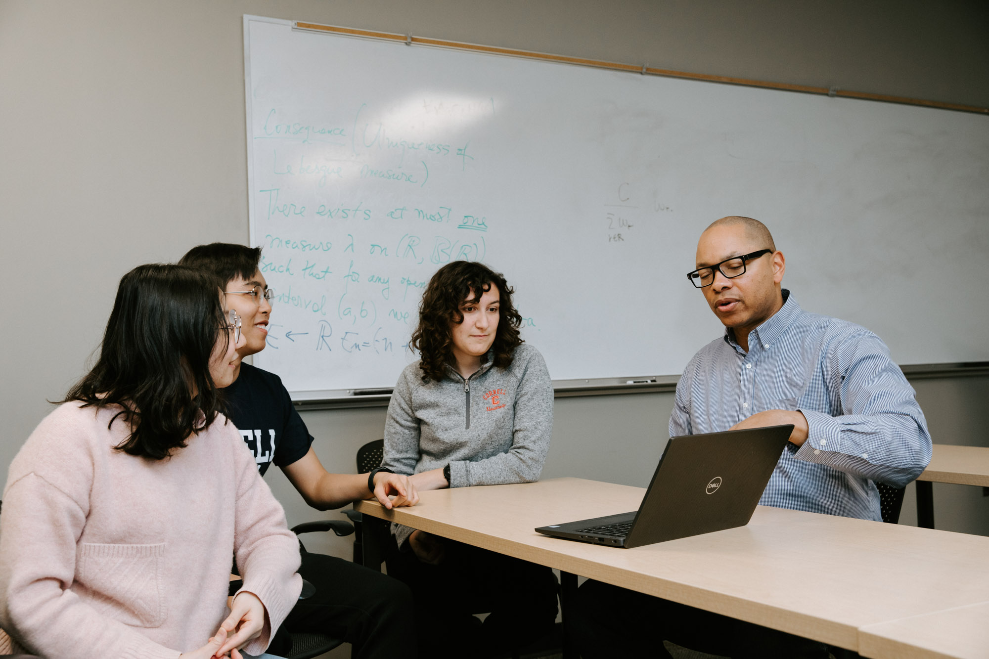 ORIE Professor Mark Lewis and three students seated in Rhodes Hall as they look at an open laptop.