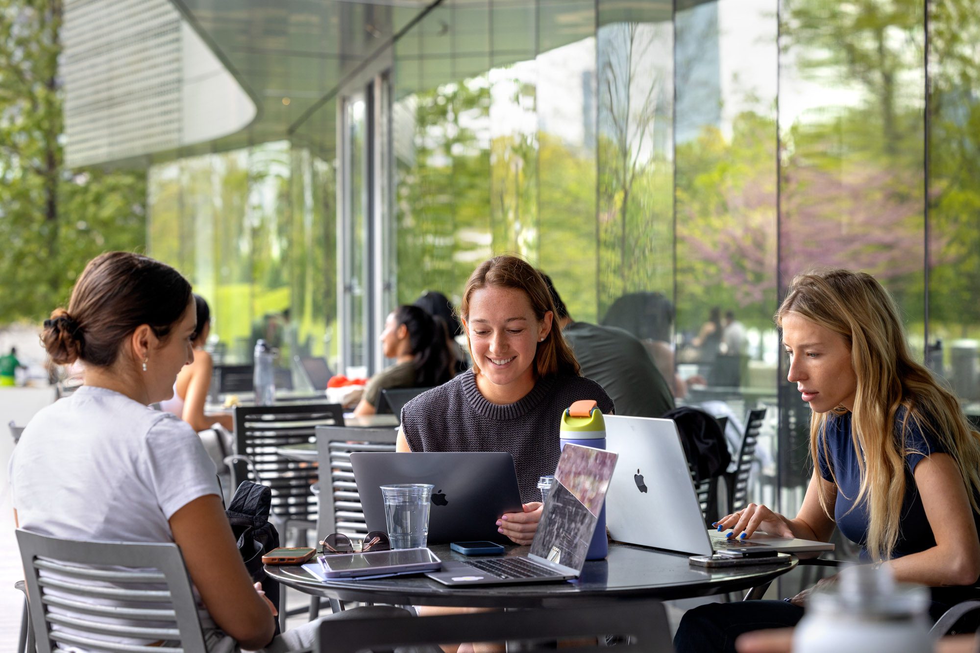 Students sit at outdoor table working on laptops
