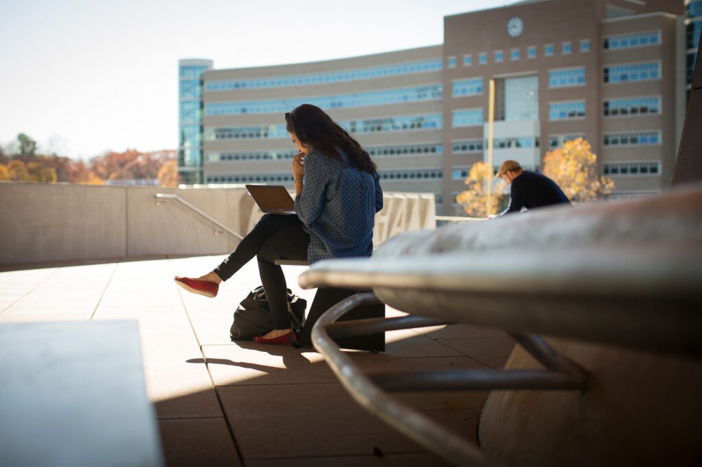 Students study outside on the Ithaca campus, with Rhodes Hall in the background.