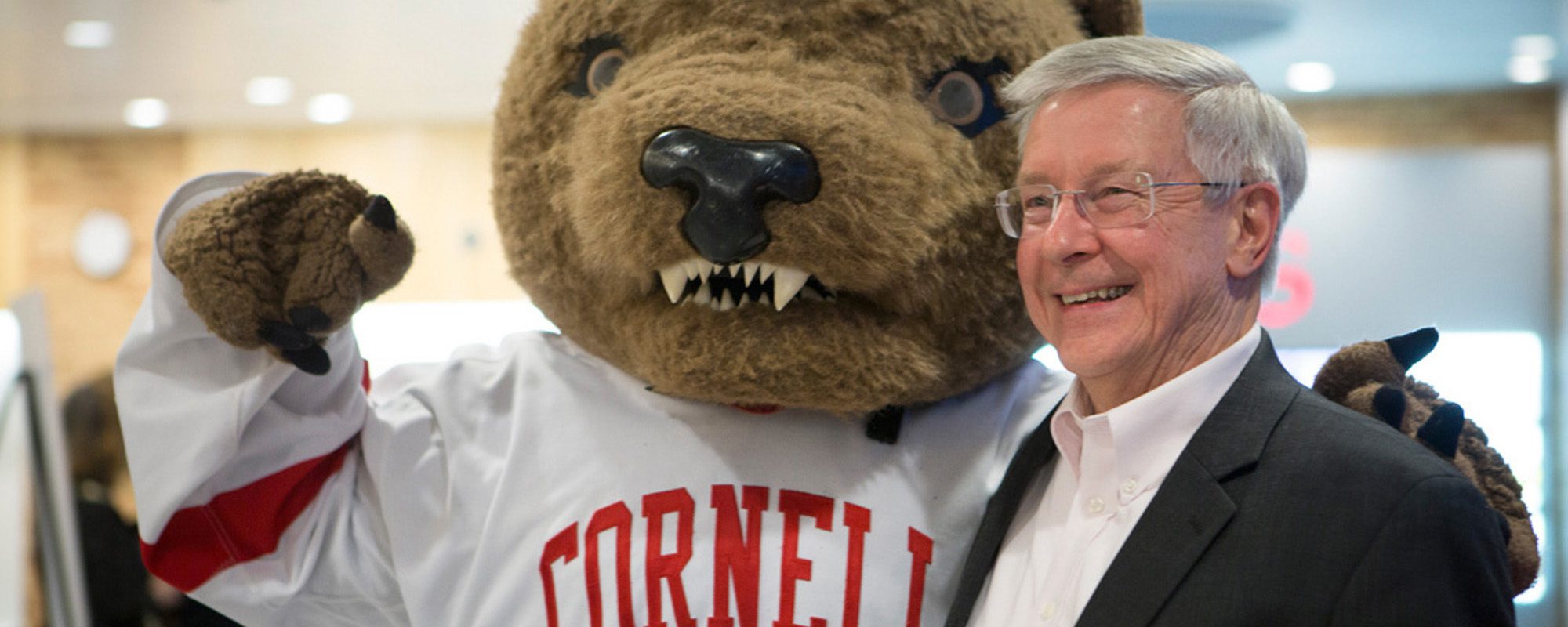 The Big Red Bear mascot stands side by side with a man in a dark blazer and white shirt.