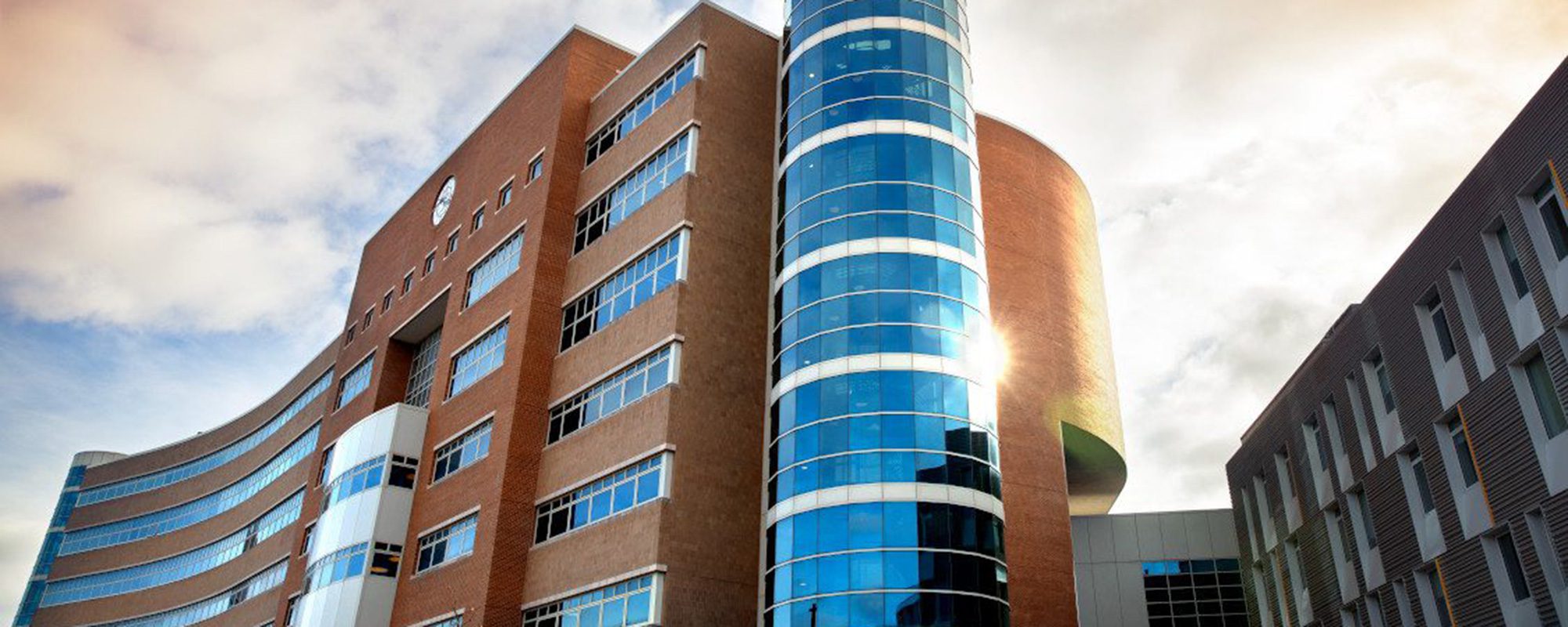 Modern, sleek and curved building with cylindrical glassy tower on the side