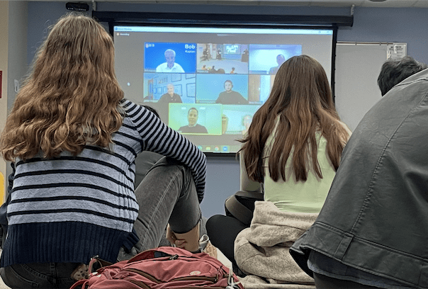 students sit on the floor and watch a Zoom webinar featuring ORIE alumni talking about their careers.