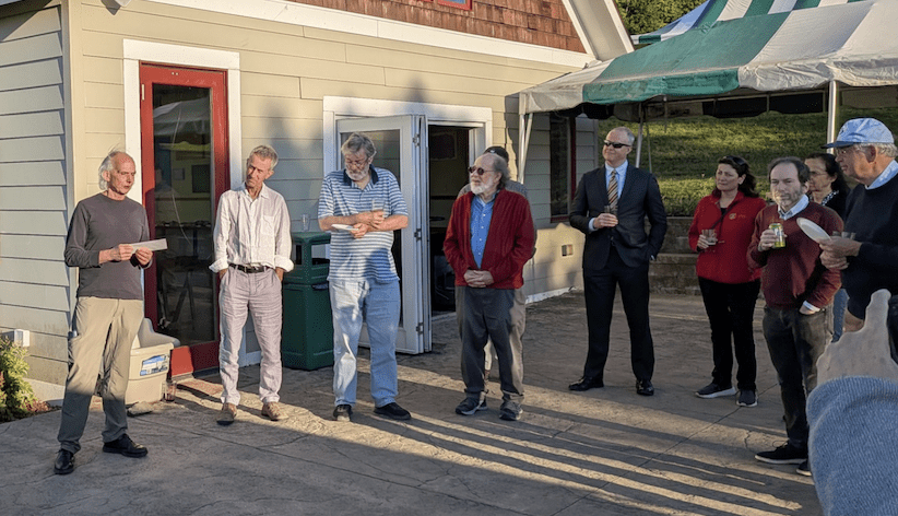 A group of people gathered on the outdoor patio of a brewery as one of the people speaks to the others.