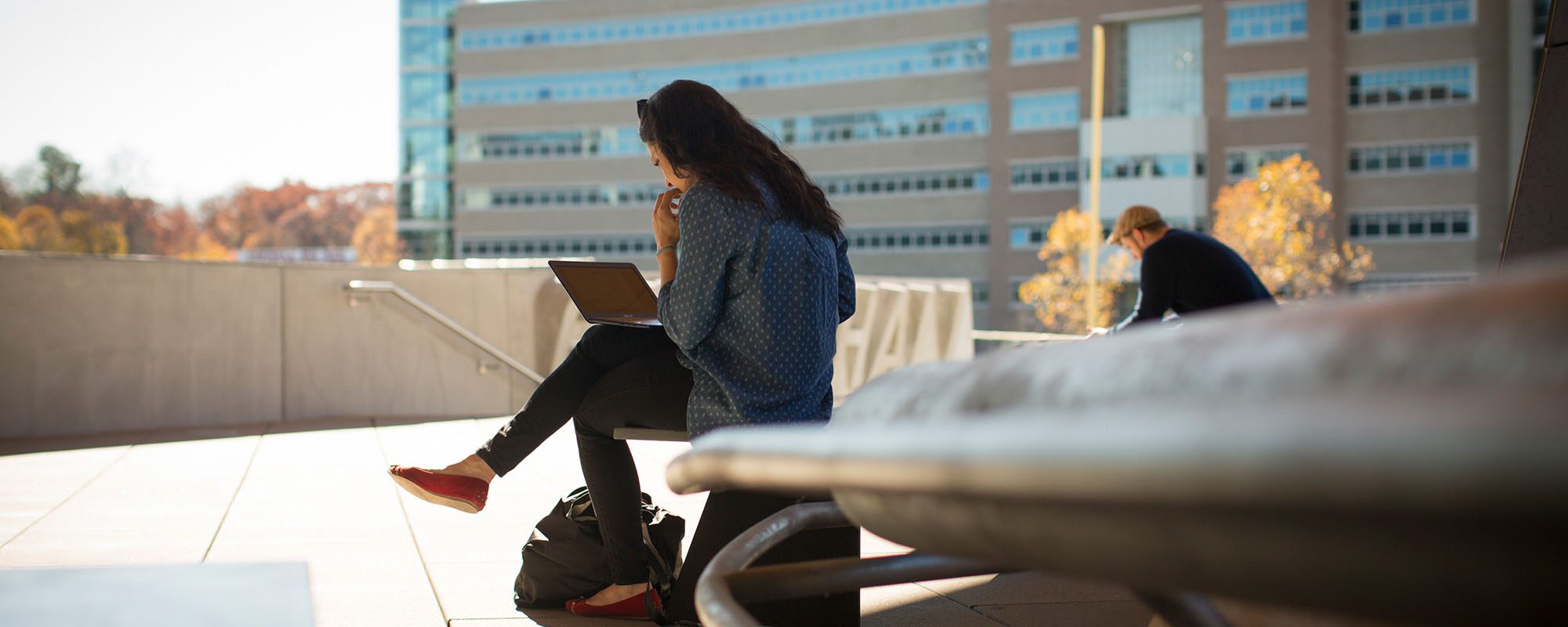Two students study outside Gates Hall in fall with Rhodes Hall in the background.