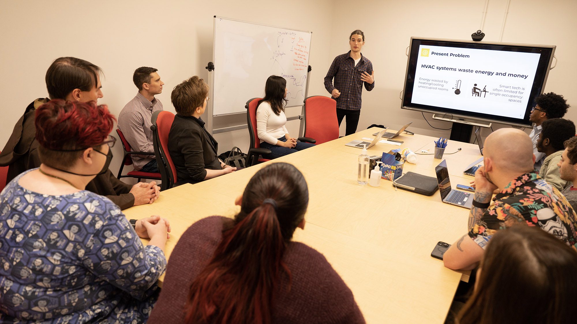 Several people sit around a table as one person gives a presentation on a screen.