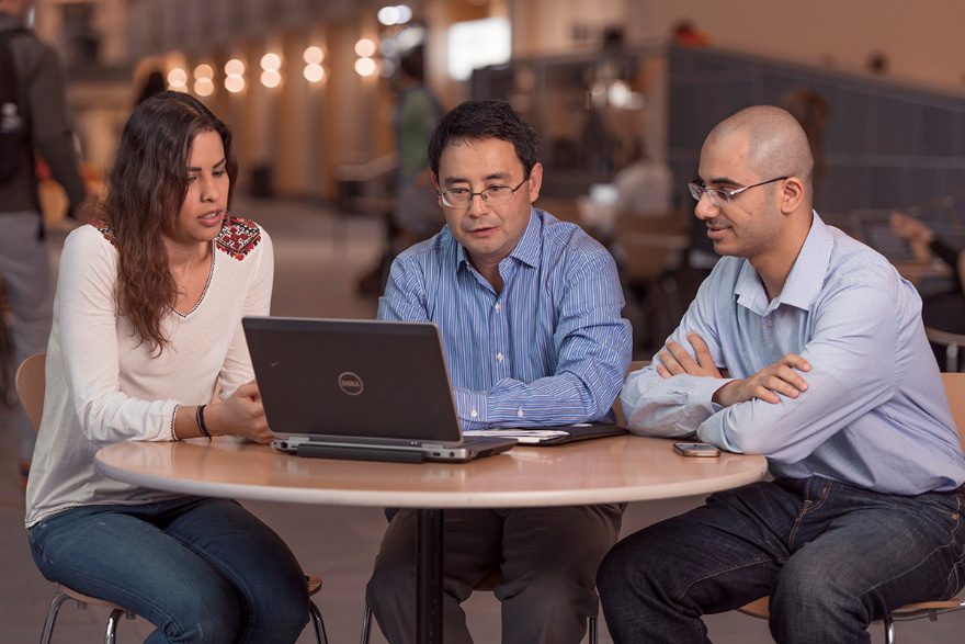 Oliver Gao sits at a table with two people, all looking at a laptop screen.