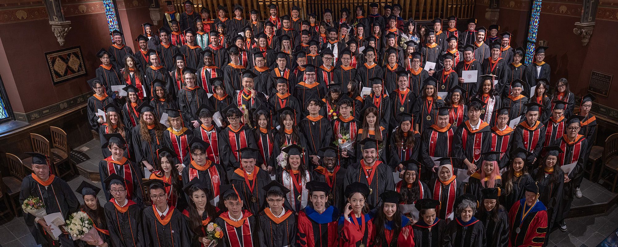 An arial group shot of a recent class of Systems Engineering graduates wearing caps and gowns and looking up at the camera.