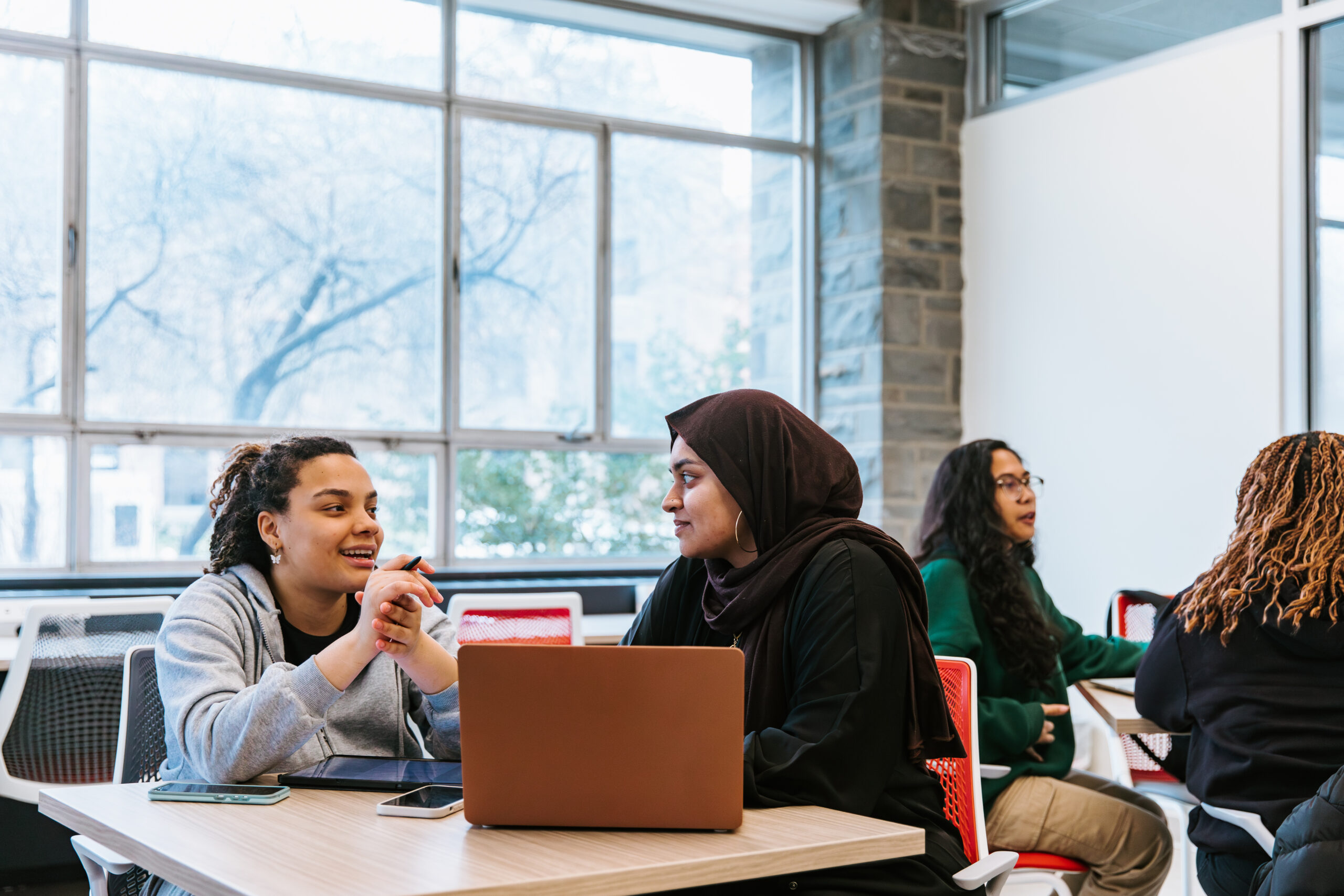Two students sit at a table and work at a laptop