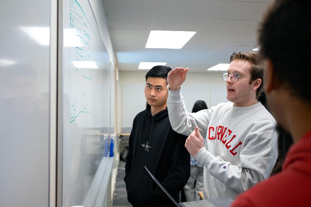 Two students stand engaged at a whiteboard