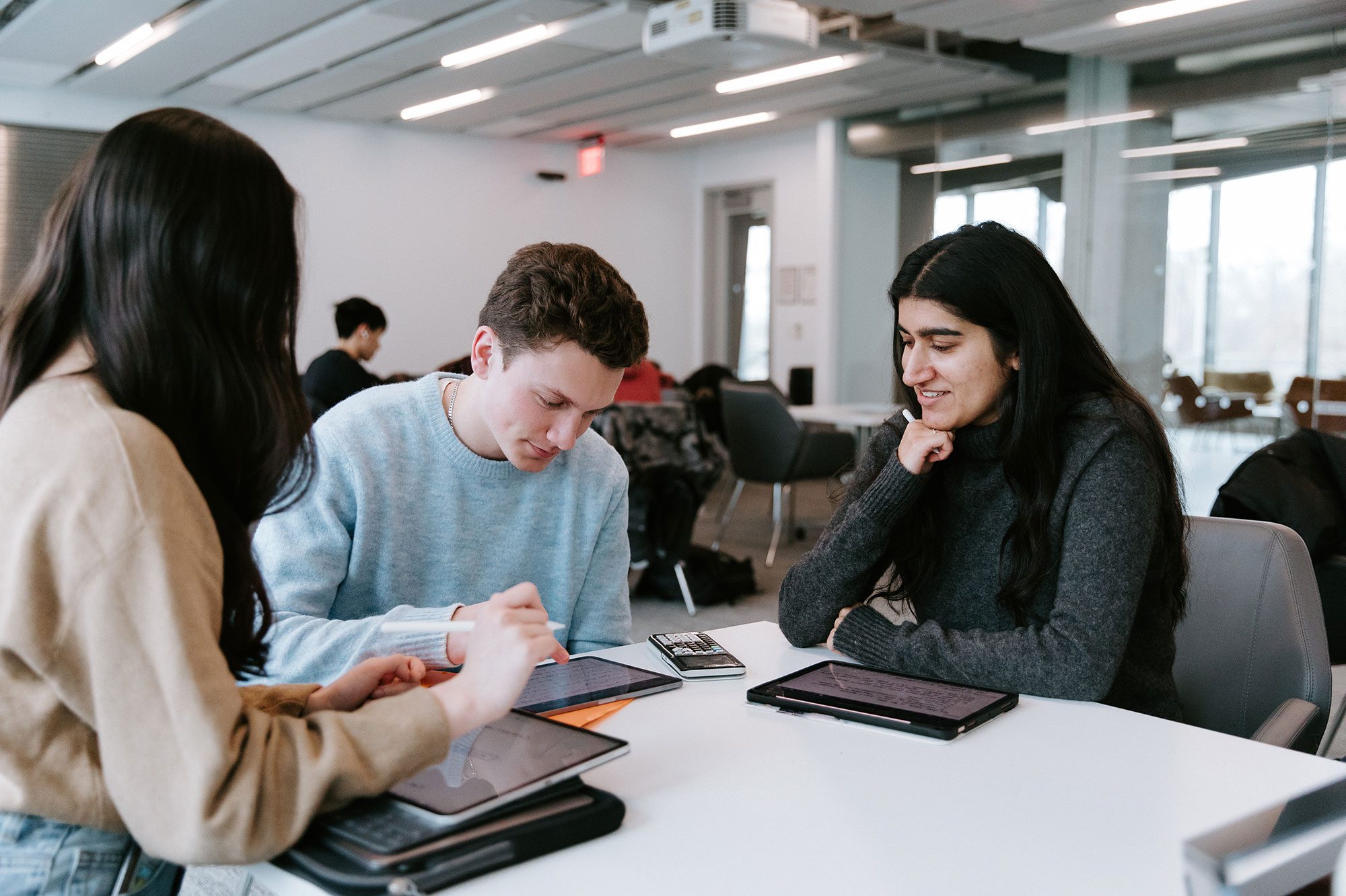 Three students work quietly on tablets together at table