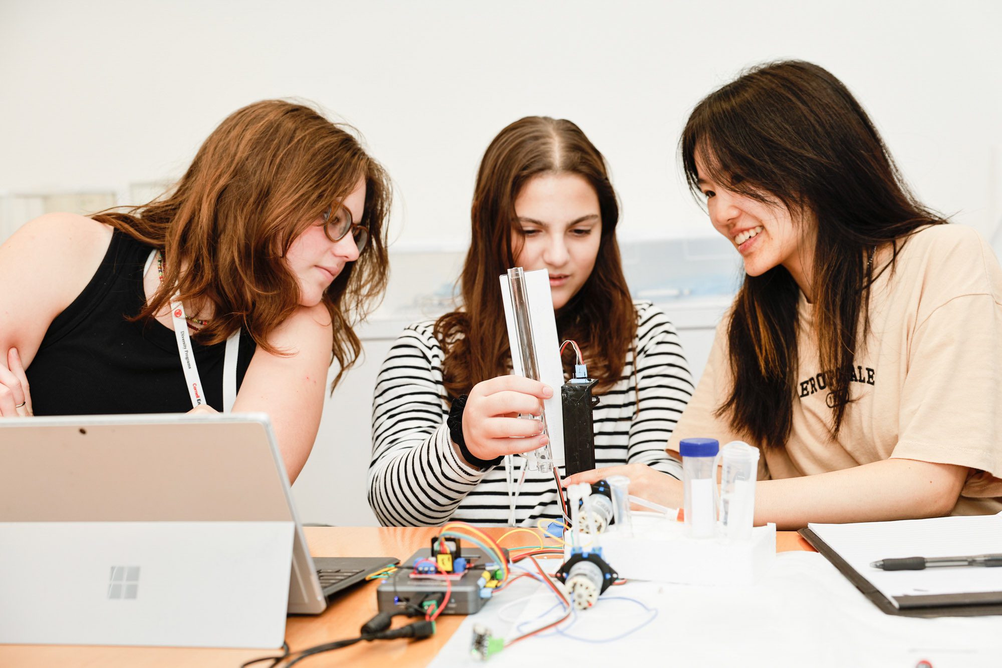 Three students work with electronic devices and computers