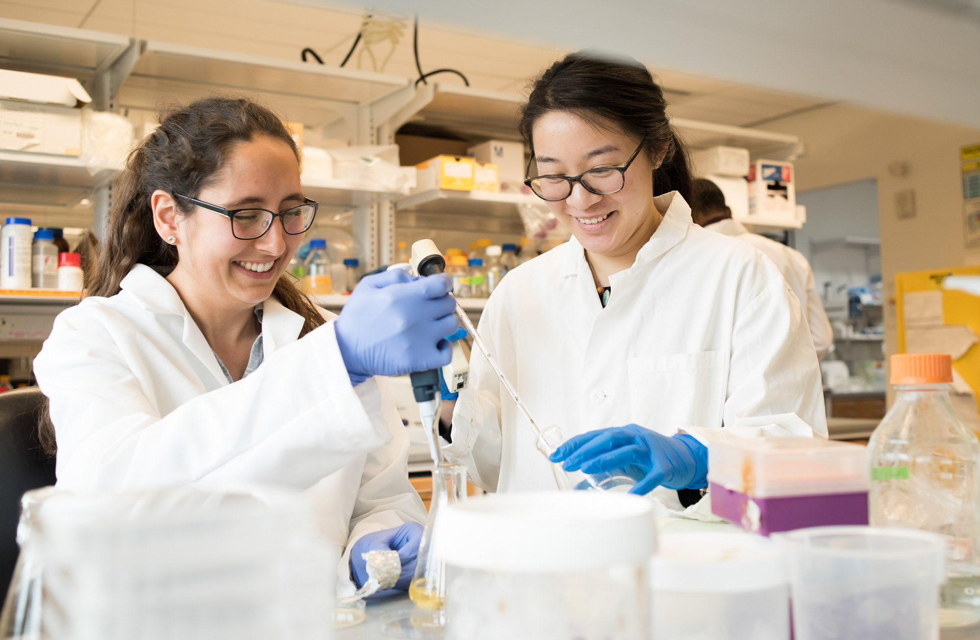 Two students in protective clothing work with equipment