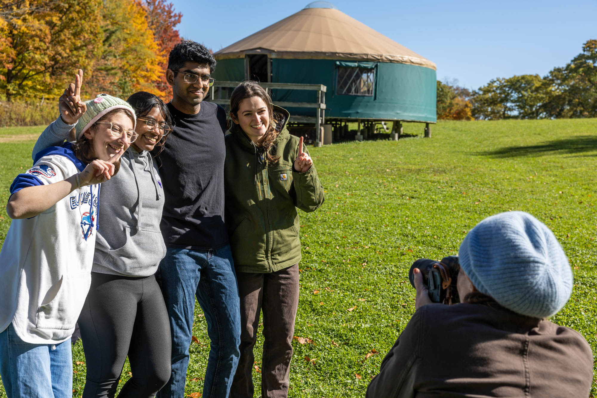 Students stand in field with arms around each other, smiling at photographer taking their photo