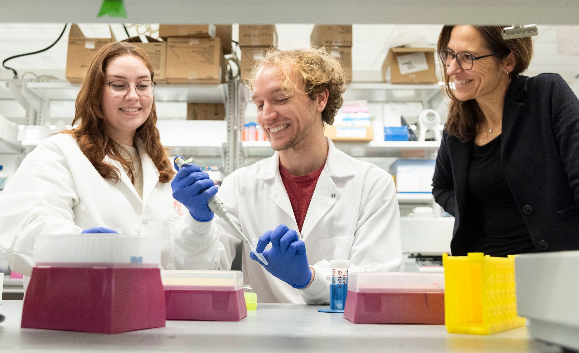Claudia Fischbach smiles while observing two researchers in lab coats