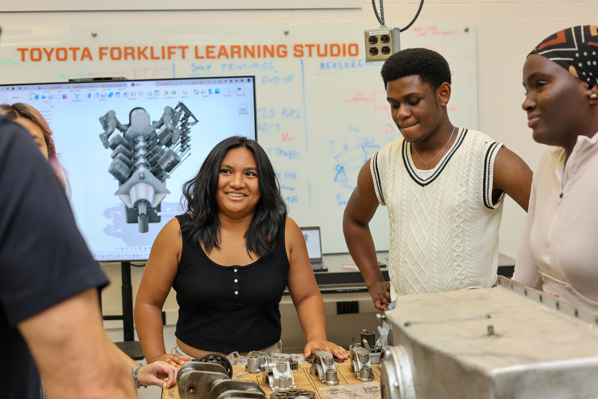 Three students stand together around forklift learning studio equipment