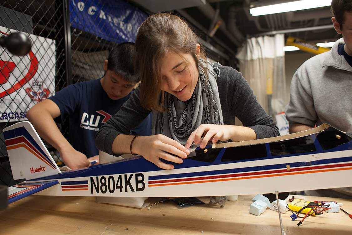 Students work on small aircrraft in large warehouse-like room