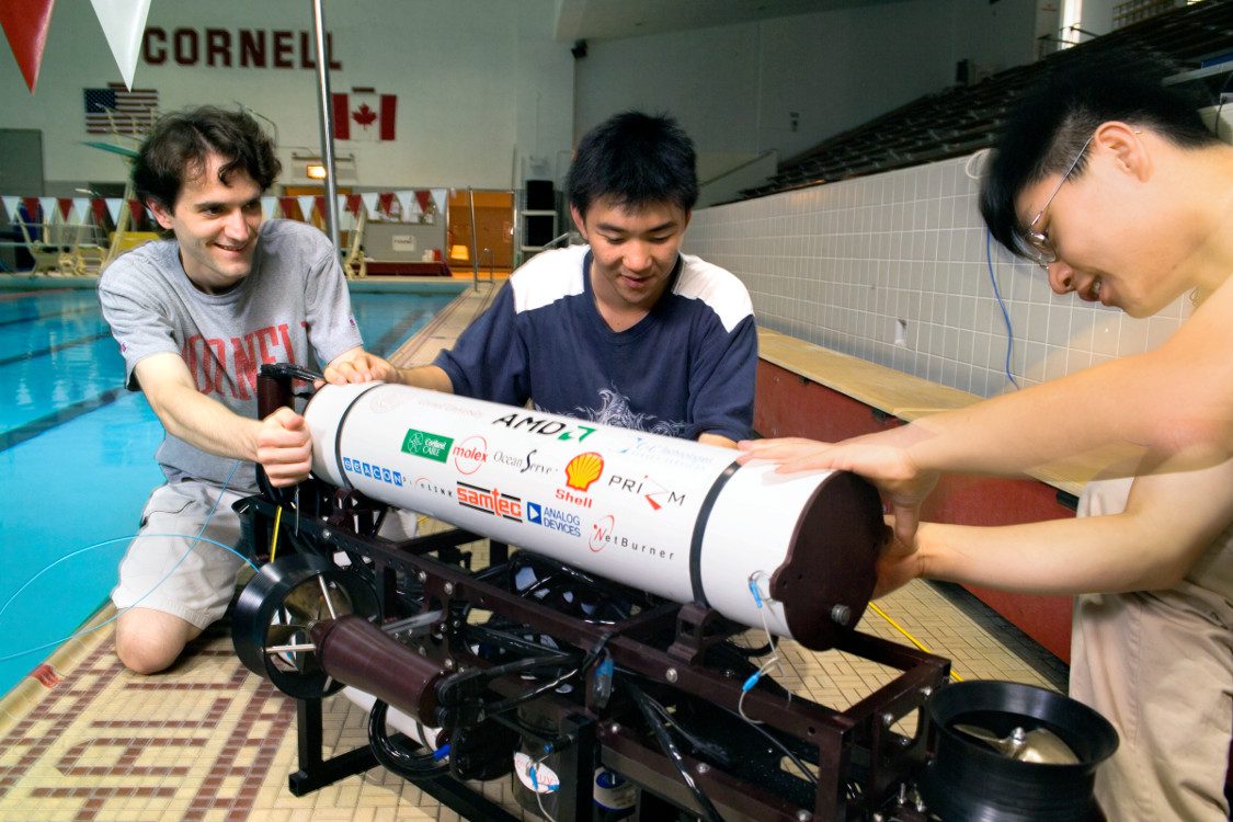 Three students work with cylindrical device by pool