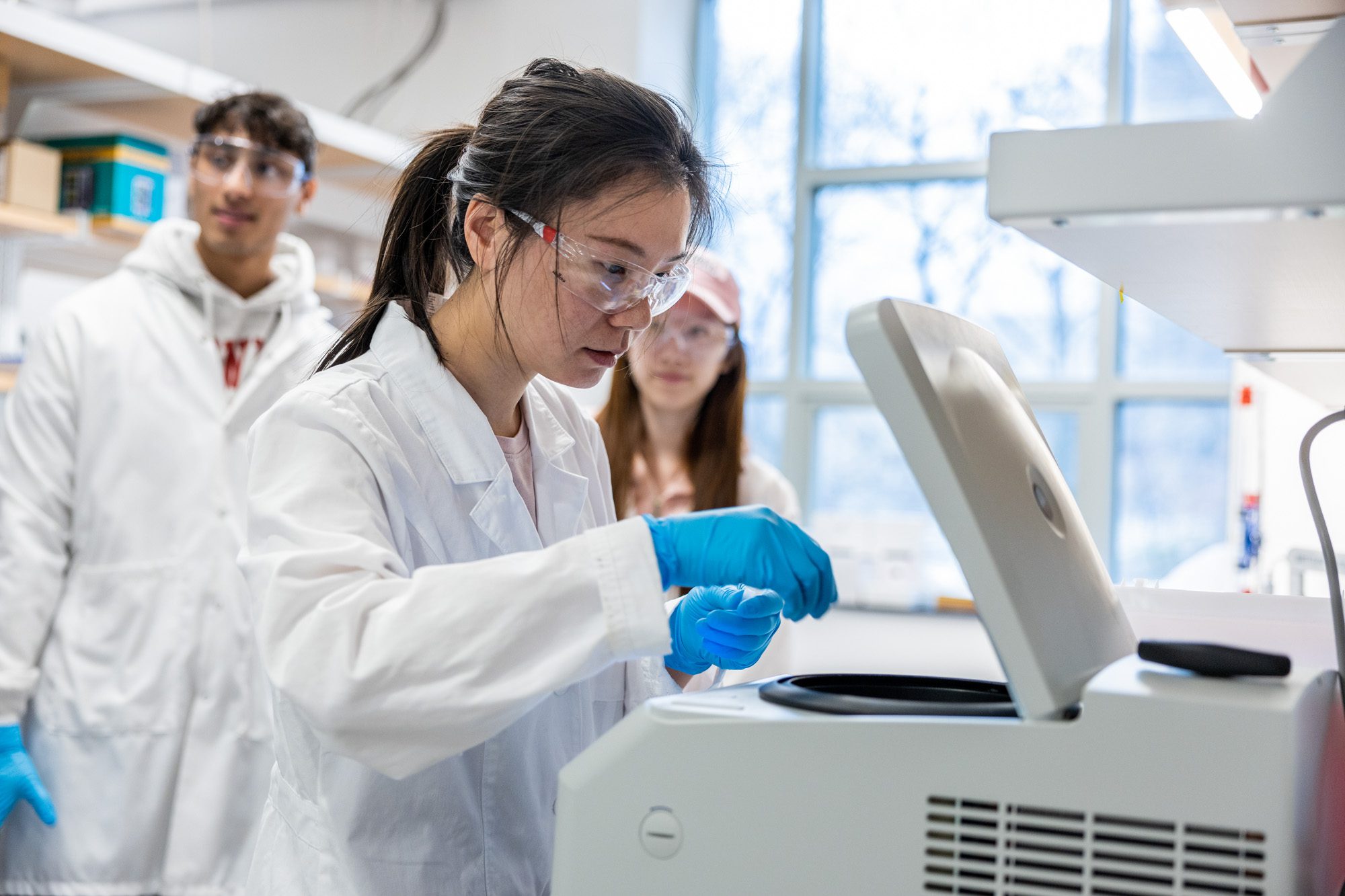 M.Eng. students in lab with white coats on and student operating machine in foreground