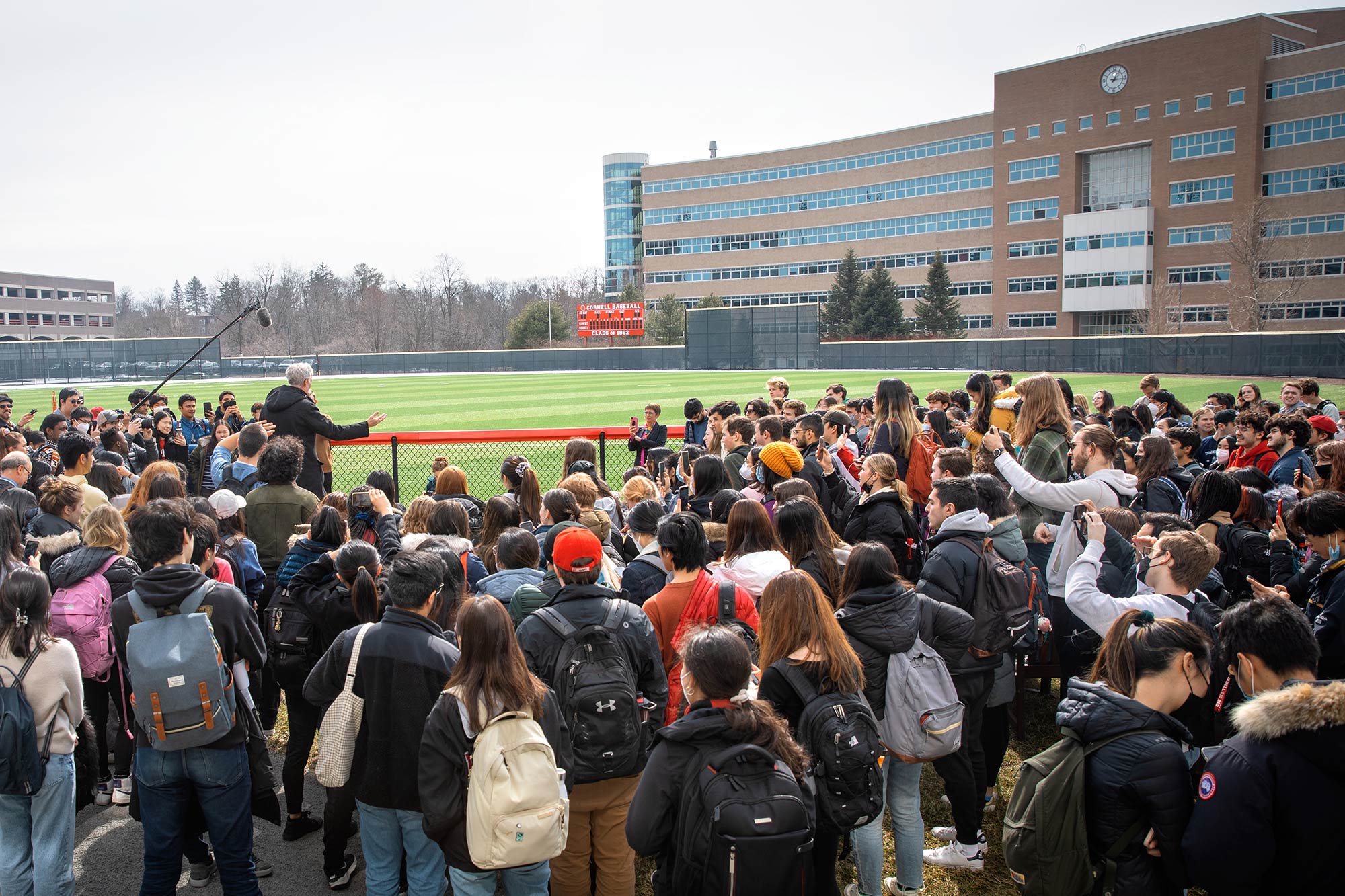 Bill Nye addressing a crowd in a green field in front of Rhodes hall