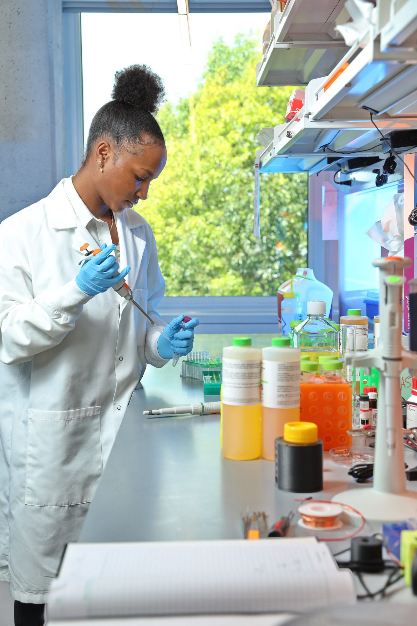 A student in lab coat and gloves uses a pipette in the lab