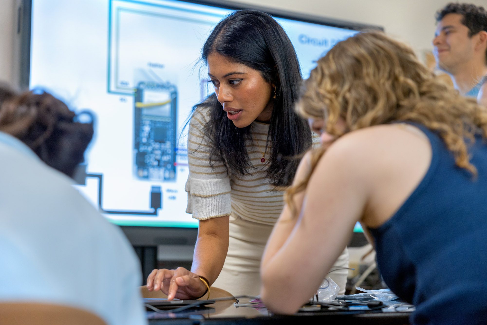 Female student showing work on a laptop to a group of people with a presentation in the background