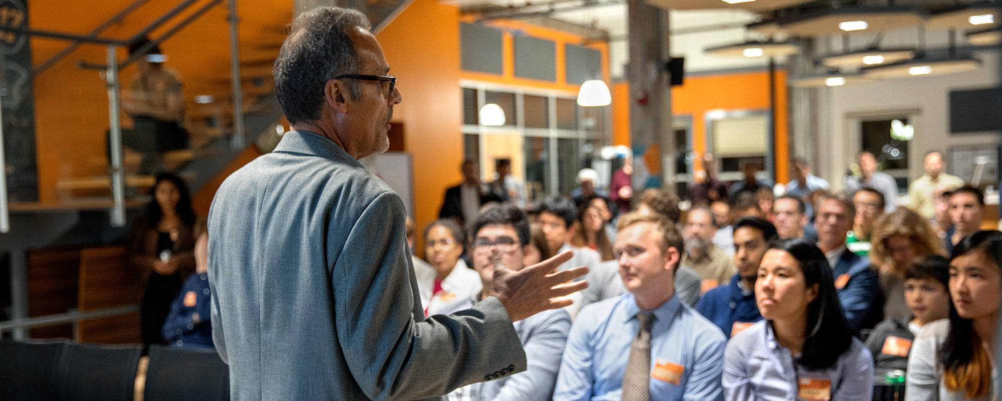 Male professor speaking in front of an audience in a dimly lit room