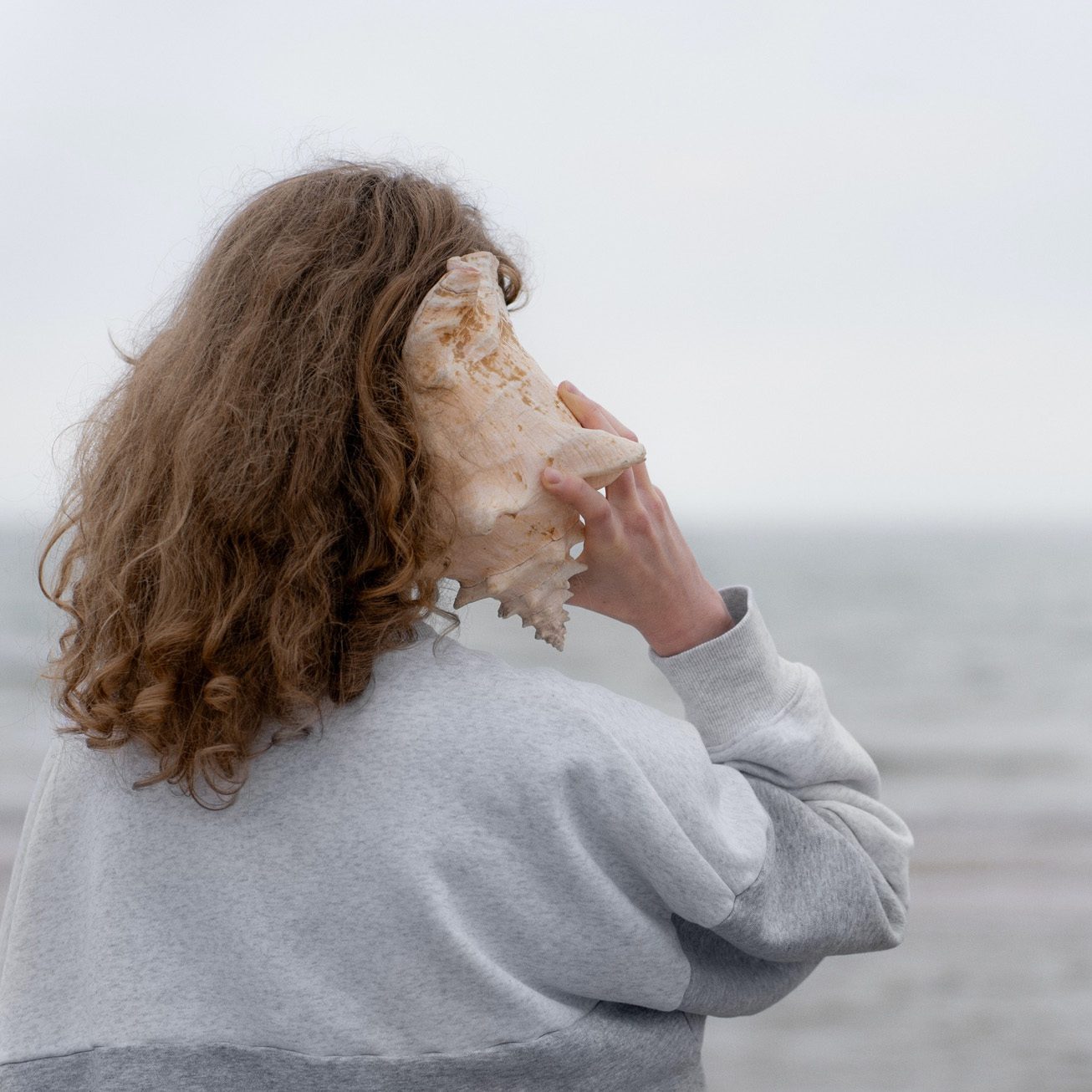 A view from the back of an individual listening to a shell.