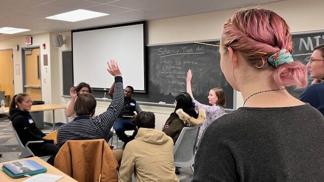 students sit in a circle in a classroom and some raise their hands