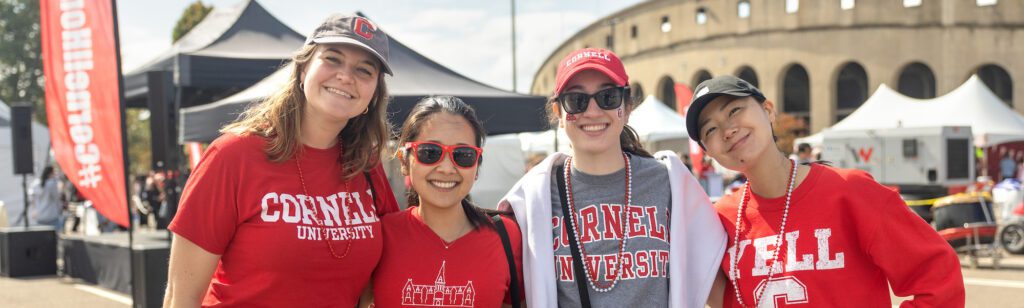 Four alumni pose in front of a stadium