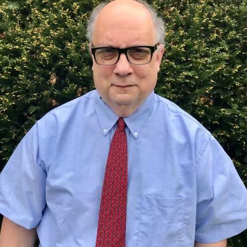 Man in glasses, shirt and red tie outside in front of greenery