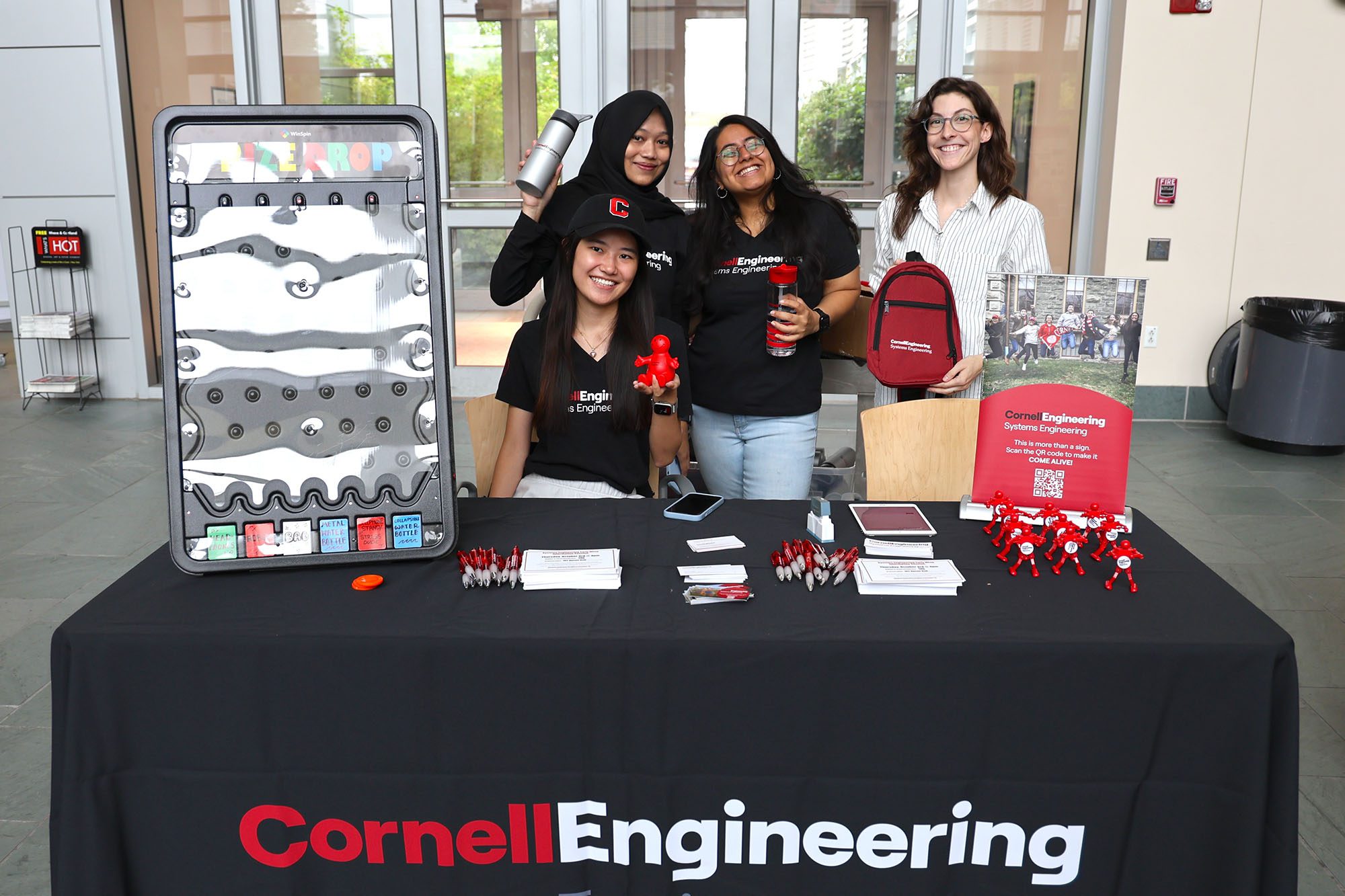 Group of students and program representatives show off prizes behind an event table at the Cornell M.Eng. Expo