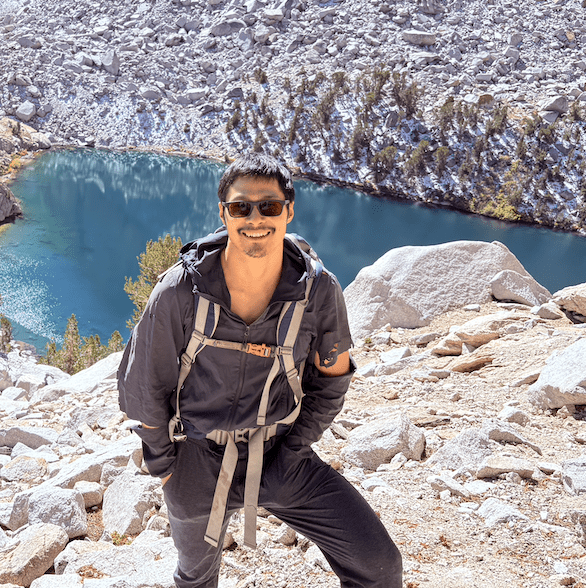 Tingan Li hiking in the mountains with a lake in the background.